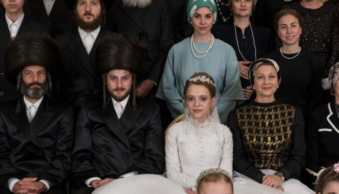 Imagen de la serie Poco Ortodoxa de Netflix. En ella se ve a la protagonista en foto familiar en el día de su matrimonio. Ella tiene una sonrisa forzada. 