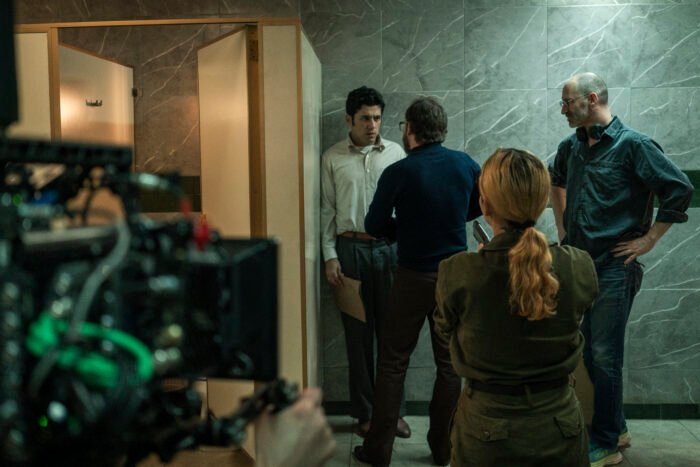 Rodaje de la película Noviembre sobre el Palacio de Justicia en Colombia: Santiago Alarcón escucha al director, Tomás Corredor, mientras el camarógrafo filma y otro miembro del equipo observa en un set de paredes grises marmóreas